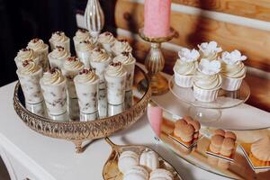 A table with a variety of desserts, including cupcakes and pastries. The desserts are arranged on a silver tray and a white table photo
