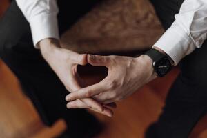 A man is sitting on a chair with his hands folded in his lap. He is wearing a watch and a white shirt. Concept of calmness and relaxation photo