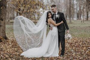 A bride and groom are standing in a field of leaves, with the bride wearing a veil and the groom holding a bouquet photo