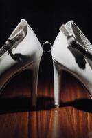 A pair of white shoes with a ring on the toe. The shoes are on a wooden table photo