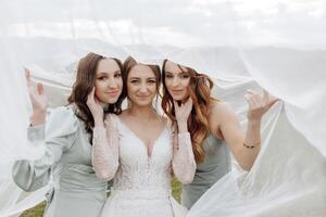 Three women are posing for a photo, with one of them wearing a wedding dress. The photo is taken from behind, with the women's faces partially hidden by a white cloth. Scene is lighthearted and fun
