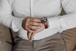 A man is wearing a watch and is checking the time. He is sitting on a couch. The watch is on his left wrist photo