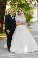 A bride and groom are posing for a picture in front of a tree. The bride is wearing a white dress and the groom is wearing a suit. Scene is happy and celebratory, as the couple is getting married photo