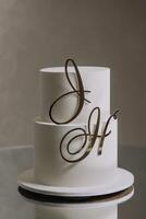 A white cake with the letters J and H on it. The cake is decorated with gold lettering and is placed on a table photo