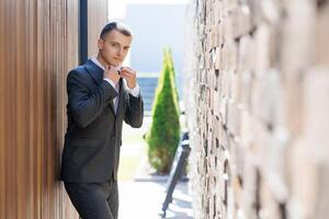 A man in a suit is standing in front of a brick wall. He is wearing a tie and he is getting ready to leave photo