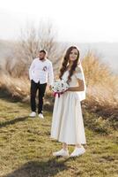 A bride and groom are standing in a field, the bride holding a bouquet. Scene is romantic and happy photo