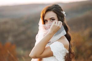 A woman is wearing a veil and standing in a field. She is looking at the camera with a smile on her face photo