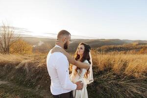 A man and woman are standing in a field, with the man hugging the woman. Scene is romantic and intimate photo