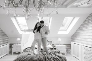 A couple is standing on a bed in a room with a chandelier above them. Scene is romantic and intimate photo