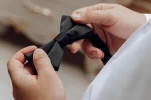 A man is holding a black bow tie and preparing to tie it. Concept of formality and elegance, as the man is getting ready for a special occasion or event photo