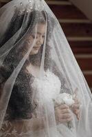 A woman is wearing a veil and holding a bouquet of flowers. She is standing in front of a staircase photo