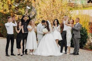 A group of people are posing for a picture, with a bride and groom in the center. The bride is wearing a white dress and the groom is wearing a suit. The group is smiling and clapping photo