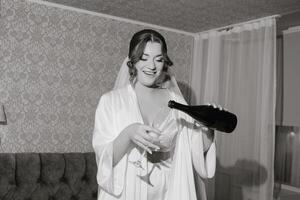 A woman in a white robe is pouring wine into a glass. She is smiling and she is enjoying the moment photo