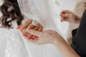 A woman is holding a ring in her hand. The ring is large and has a diamond on it. The woman is wearing a white dress, and the scene appears to be a wedding or a special occasion photo