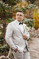 A man in a suit and tie stands in front of a tree. He is holding a bouquet of flowers in his hand photo