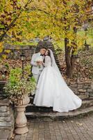 A bride and groom are posing for a picture in front of a tree. The bride is wearing a white dress and the groom is wearing a suit. They are both smiling and hugging each other photo