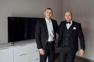 Two men in suits are standing next to each other in a room. One of them is wearing a tie photo