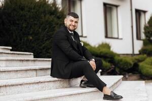 A man in a suit is sitting on a set of stairs. He is smiling and he is enjoying himself photo