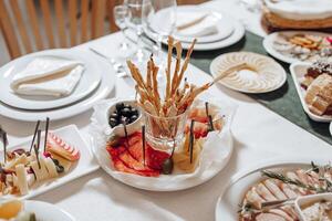 A table with a variety of food, including a plate of breadsticks and a bowl of olives photo