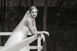 A bride is standing on a bridge with her back to the camera. She is wearing a white dress and a veil photo
