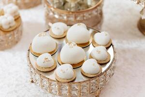 A tray of white pastries with gold accents. The tray is on a table and the pastries are arranged in a circle photo