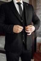 A man in a black suit is getting ready for a formal event. He is adjusting his tie and checking his appearance in the mirror. Concept of professionalism and sophistication photo