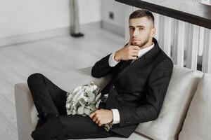 A man in a suit is sitting on a couch with a bouquet of flowers in his lap photo