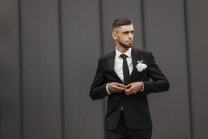A man in a suit and tie is standing in front of a wall. He is adjusting his tie and holding a flower in his hand. Concept of formality and elegance, as the man is dressed in a suit photo