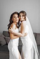 Two women in white dresses are hugging each other photo