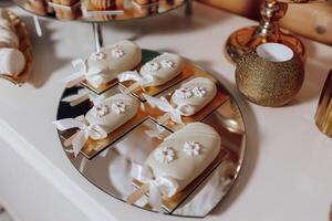 A table with a white plate of pastries with white bows on them. The pastries are decorated with white frosting and are arranged in a circular pattern photo