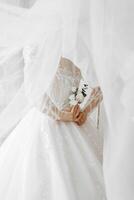 A woman in a white wedding dress is holding a bouquet of flowers. The woman is standing in front of a curtain, which is partially covering her photo
