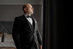 A man in a suit and tie stands in front of a window. He is looking out of the window, possibly waiting for someone or just taking a break from work. Concept of formality and professionalism photo