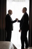 Two men shaking hands in a hotel room. Scene is professional and formal. The idea of the image is that of two men shaking hands, possibly in a business setting photo