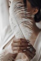 A woman is holding a feather in her hand. The feather is white and has a delicate, elegant appearance. The woman's hand is positioned behind the feather, creating a sense of mystery and intrigue photo
