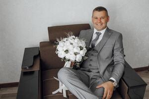 A man in a suit and tie is sitting on a couch holding a bouquet of flowers. Concept of elegance and sophistication, as the man is dressed in formal attire photo