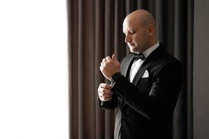 A man in a suit is getting ready to wear a bow tie. He is adjusting it and looking at the camera. Concept of formality and attention to detail photo