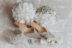A pair of high heels and a bouquet of white flowers are displayed on a bed. The shoes are adorned with glitter and the flowers are fresh and white. Concept of elegance and sophistication photo