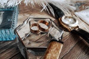 A pair of gold wedding rings are displayed in a clear case on a wooden table. A watch is also present on the table. Concept of love and commitment, as the rings symbolize a lifelong partnership photo