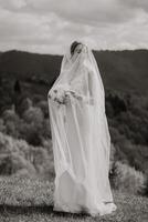 A bride is standing in a field with a veil covering her face. She is holding a bouquet of flowers photo