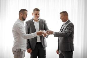 Three men in suits are toasting each other with glasses of wine. Scene is celebratory and friendly photo