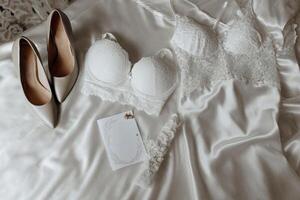 A pair of high heels and a bra are on a bed. The bra is white and the shoes are silver photo