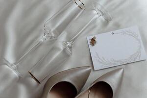 A pair of high heels and two champagne flutes are on a bed. The champagne flutes are gold and the shoes are white photo