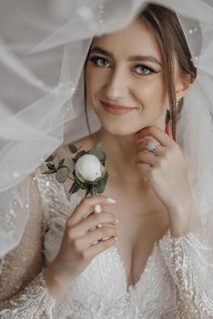 A woman is wearing a white dress and holding a flower in her hand. She is smiling and looking at the camera photo