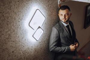 A man in a suit stands in front of a lighted square sign. He is wearing a tie and he is posing for a photo