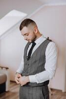 A man in a suit and vest is standing in front of a wall. He is wearing a tie and he is adjusting it. Concept of formality and professionalism, as the man is dressed in a suit and vest photo