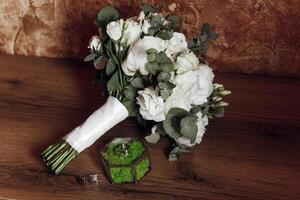 A bouquet of white flowers sits on a wooden table next to a small glass vase. The flowers are arranged in a way that they look like they are about to be used for a wedding photo