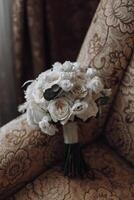 A bouquet of white flowers sits on a chair. The flowers are arranged in a way that they look like they are about to be given as a gift. The chair is covered in a patterned fabric photo