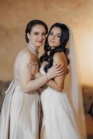 Two women are hugging each other, one of them is wearing a wedding dress. Scene is warm and affectionate photo