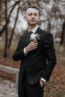 A man in a suit holding a flower in his hand. Concept of elegance and sophistication, as the man is dressed in a tuxedo and holding a flower. The flower adds a touch of natural beauty to the scene photo