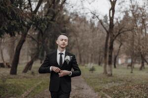 A man in a suit is walking through a park, holding a bouquet of flowers. The scene is serene and peaceful, with the man looking into the distance photo